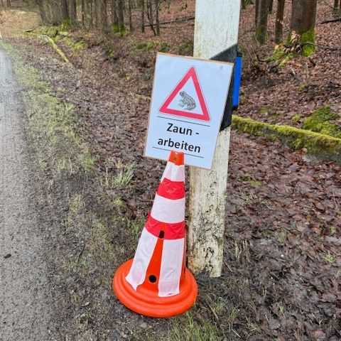 Warnschild und Pylone sichern die Arbeiten am Straßenrand ab.